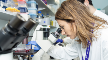 A female researcher wearing a lab coat looking down a microscope