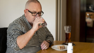 Man drinking water as he takes PERT and eats a sandwich