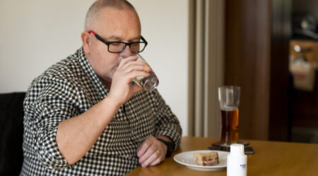 Man drinking water as he takes PERT and eats a sandwich
