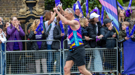 Person in a Pancreatic Cancer UK top running with arms raised past a cheering crowd