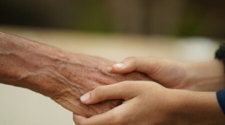 A child's hands gently clasp an older person's hand.