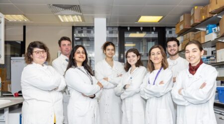 Researchers in lab coats standing in a line with their arms crossed.