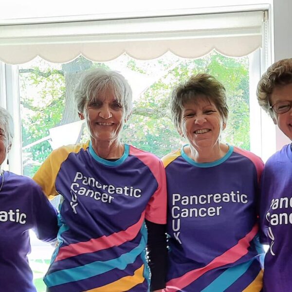 A group of women in purple t-shirts stood around a table, filled with cakes