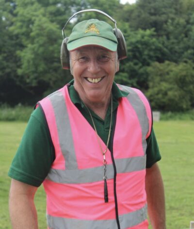 A man in a high-visibility vest and ear defenders smiles on a clay pigeon shoot