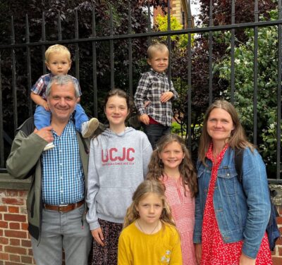 A mum, dad and their five young children smile on a sunny day.