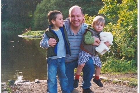 Man kneeling with one young child on his knee and the other standing beside him with his arm around his neck