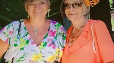 Mother and daughter standing with arms around each other wearing brightly coloured dresses for a summer wedding