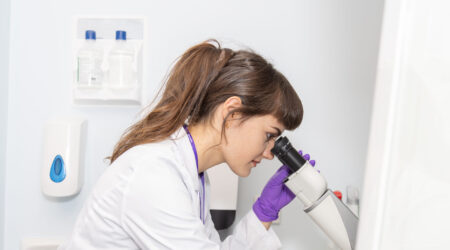 woman in a white coat looking down a microscope