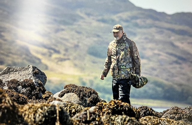 A man with a large camera walks in a rugged landscape