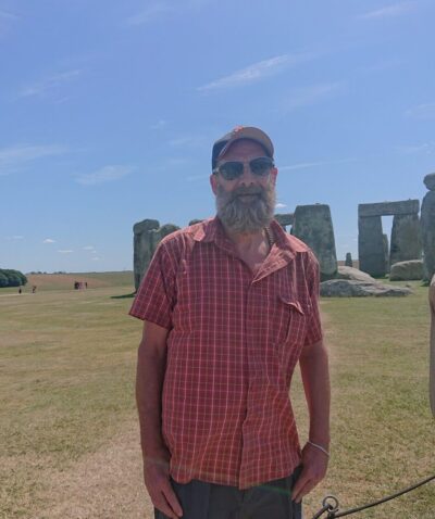 Man standing in front of Stonehenge, wearing cap and sunglasses