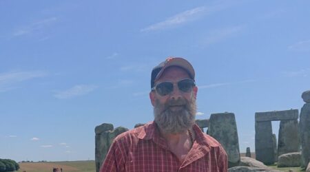 Man standing in front of Stonehenge, wearing cap and sunglasses