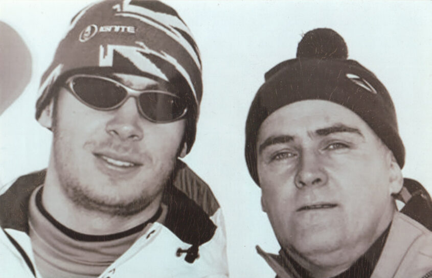 Lewis, a young man with sunglasses and a wooly hat on stands next to his late dad, Jeff who is also wearing a wooly hat.