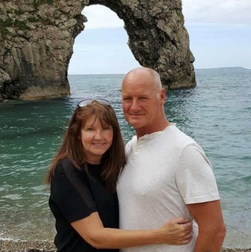 Man and woman holding each other in front of the sea and cliff arch