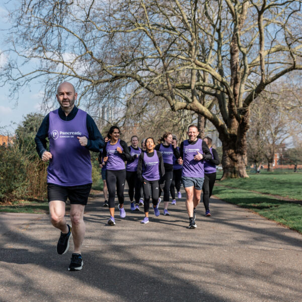 A group of runners, wearing Pancreatic Cancer UK jerseys, runs through a park. Graham Sturge leads the way.