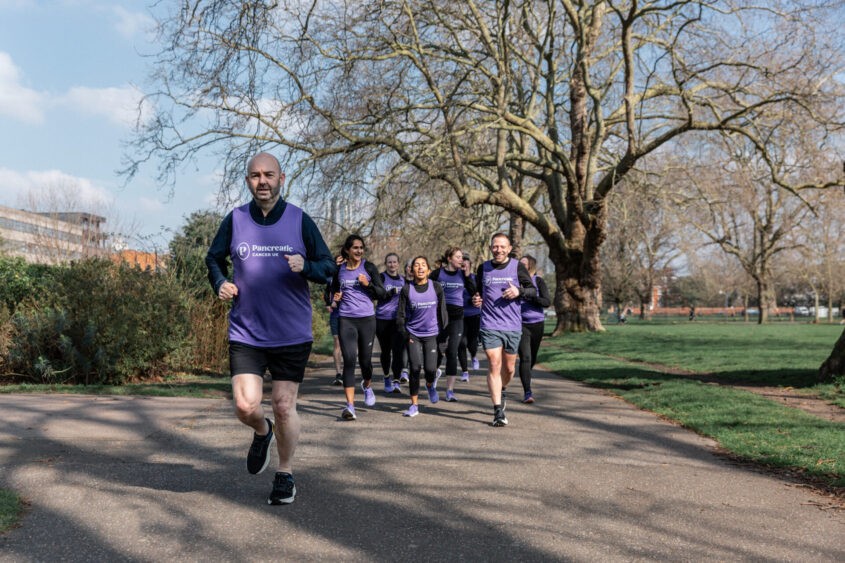 A group of runners, wearing Pancreatic Cancer UK jerseys, runs through a park. Graham Sturge leads the way.