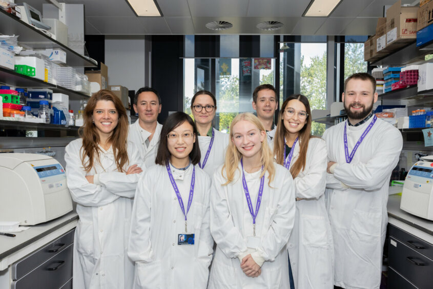 Group of researchers in lab coats smiling and folding their arms