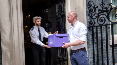man wearing a white shirt handing a box to a officer at downing street