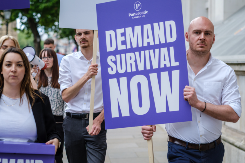 men and women walking down the street with signs one reading demand survival now