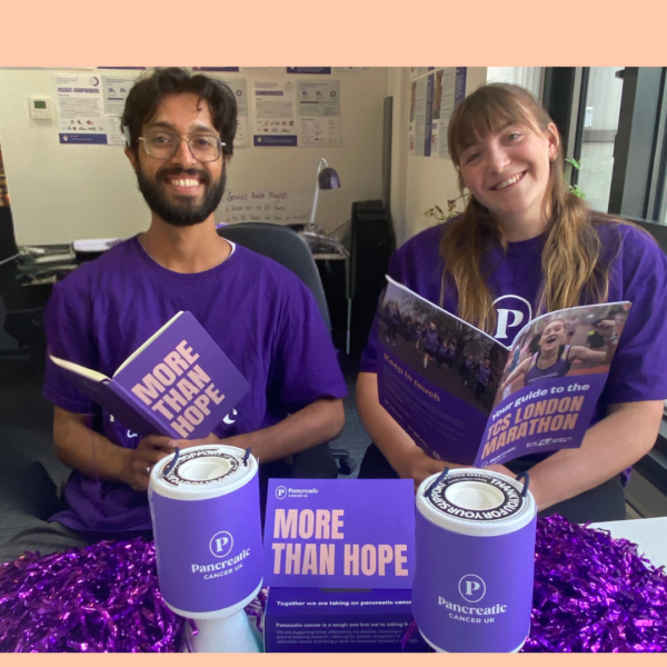 two people smiling at the camera with fundraising materials and collection tins in front of them