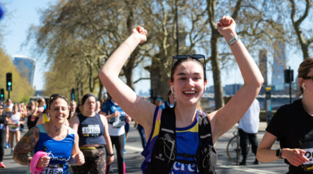 Woman in Pancreatic Cancer UK vest running and cheering with her hands up