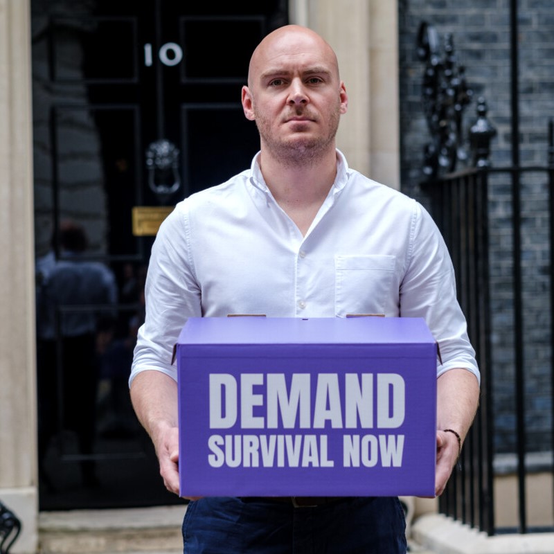 Lewis outside Numer-10 Downing Street Demand Survival Now campaign