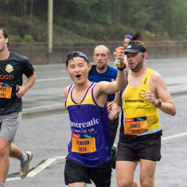 Runner in Pancreatic Cancer UK vest running and holding a packet of sports gel