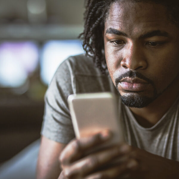 Young man looking seriously at his phone lying down on his front