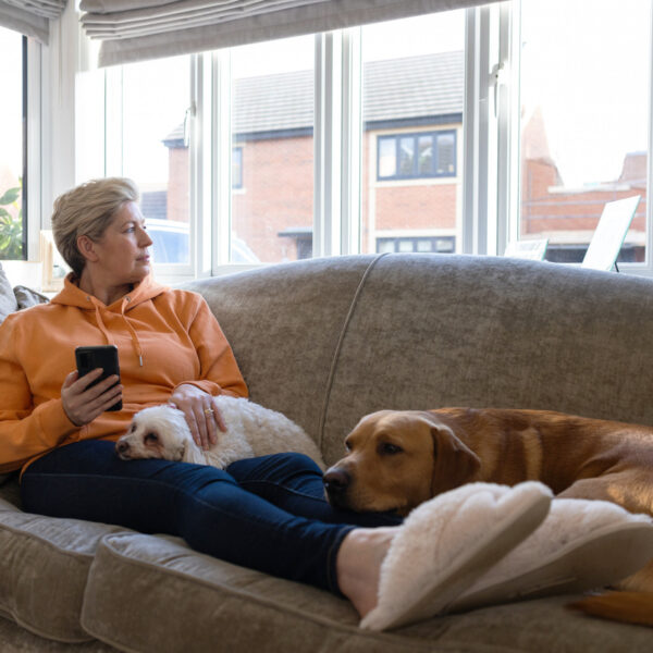 A middle aged woman layin on her sofa with her dog looking out the living room window