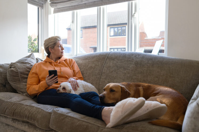 A middle aged woman layin on her sofa with her dog looking out the living room window
