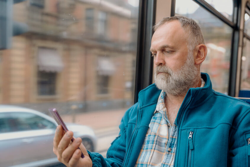 A man sitting on a bus looking at his phone