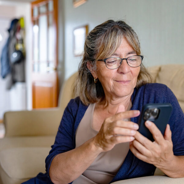 Older woman sitting in her living room looking at her phone and smiling slightly