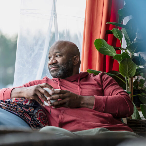 Middle aged man holding a cup looking out of a living room window