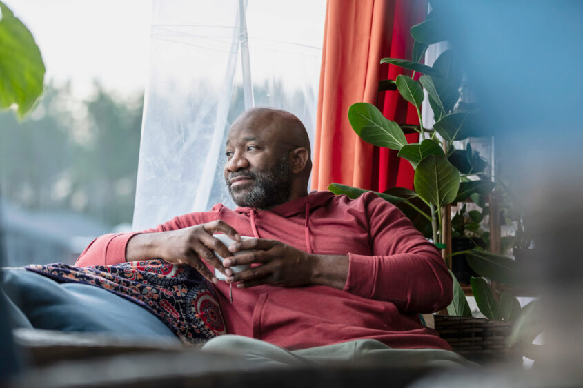 Middle aged man holding a cup looking out of a living room window
