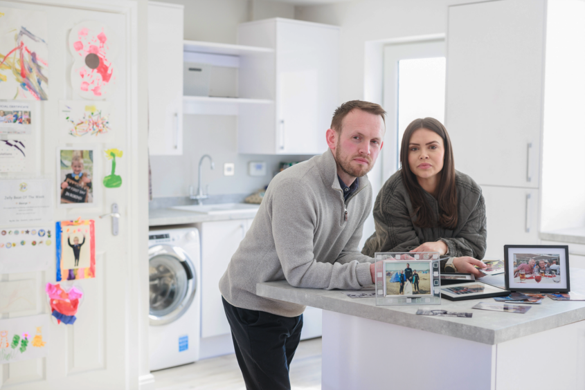 David and Lucy Orchard, standing in a kitchen in front of photos of dad on the counter
