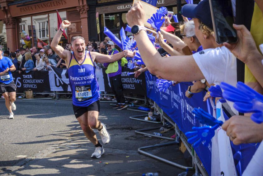 A runner wearing a PCUK vest with his fist in the air as he runs along a PCUK cheer point
