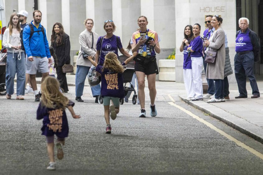 Two young girls running to greet a woman wearing a PCUK running vest