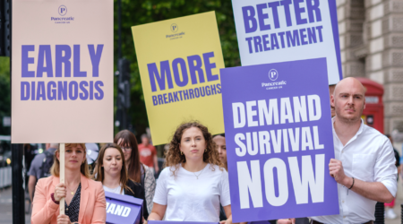 Team of PCUK staff with signs saying 'early diagnosis', 'more breakthroughs', demand survival now' and 'better treatment', walking towards Downing Street.