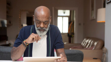 Older man sitting at table at home reading from a tablet device