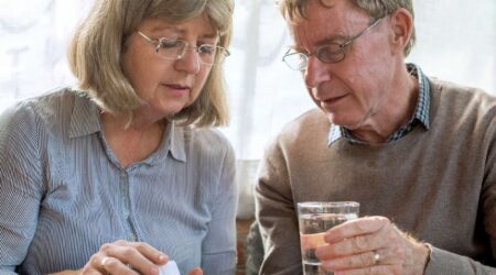 Woman giving man tablets into his hand, he's holding a glass of water in the other hand