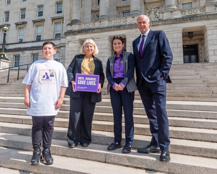A young boy stands with three adults on the stairs outside Stormont. One holds a sign calling for early detection of pancreatic cancer