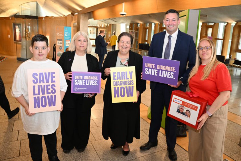 A group of five stand inside Holyrood, holding signs calling for the early detection of pancreatic cancer to save lives