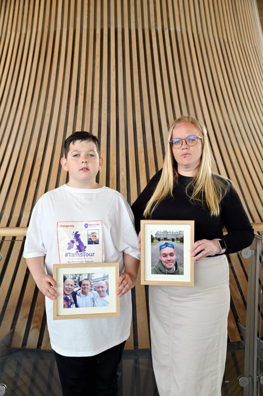 Young boy stands next to his aunt who holds a photo of her brother who lost his life to pancreatic cancer