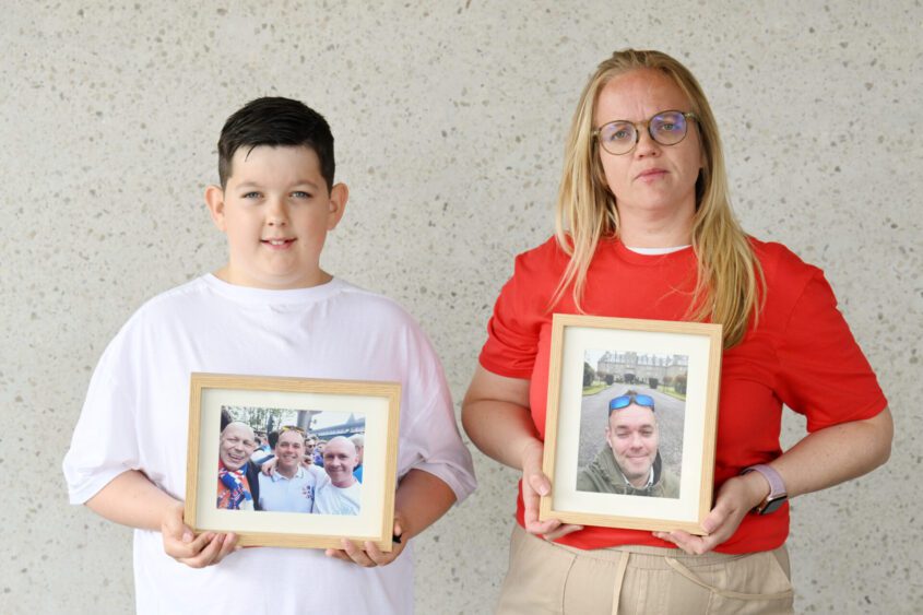 A boy holding a photo of his dad, who died from pancreatic cancer, stands next to his aunt. She also holds a photo of her late brother