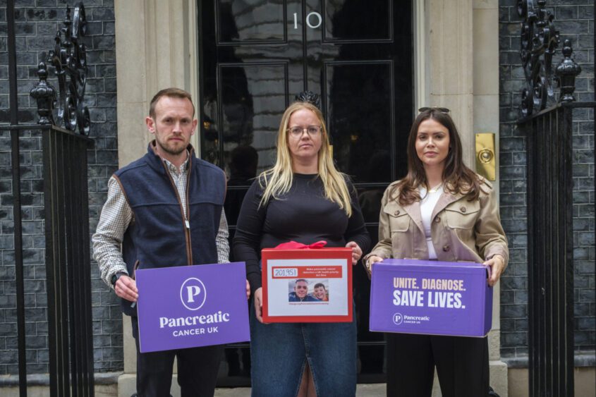 A man and two women stand outside Number 10, Downing Street with petition boxes that contain signatures calling for early detection of pancreatic cancer