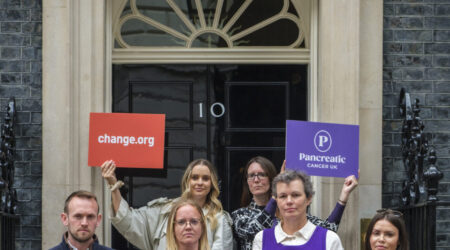 Group of six people stand outside Number 10, Downing Street. Two people at the back hold signs calling for early detection of pancreatic cancer. Two people at the front hold boxes that include signatures from people calling for early detection.