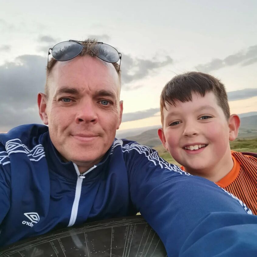 A man stands next to his young son, smiling