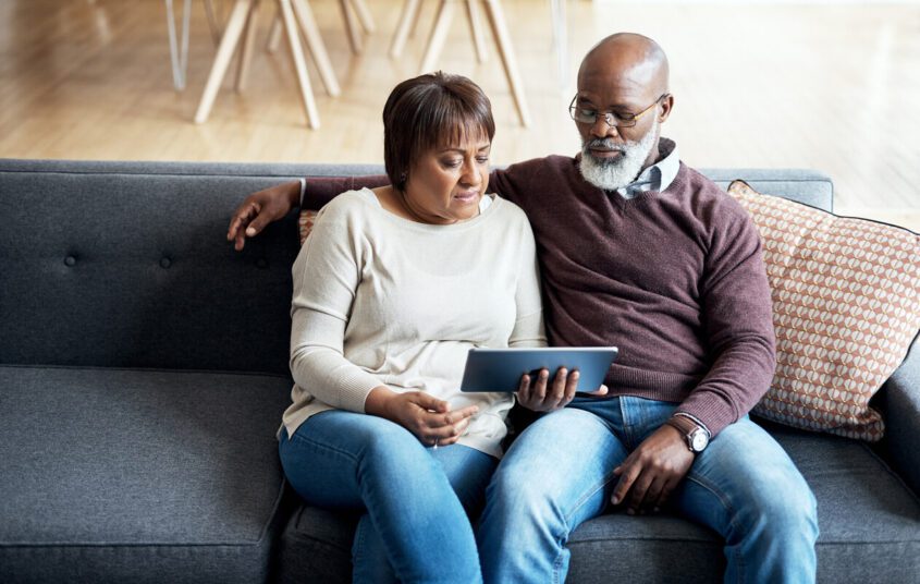 Couple sitting on sofa looking at a tablet together.