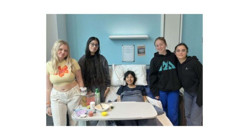 Young woman lying in hospital bed surrounded by 4 friends