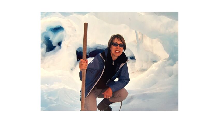 woman on a snowy mountain holding a walking pole, wearing sunglasses