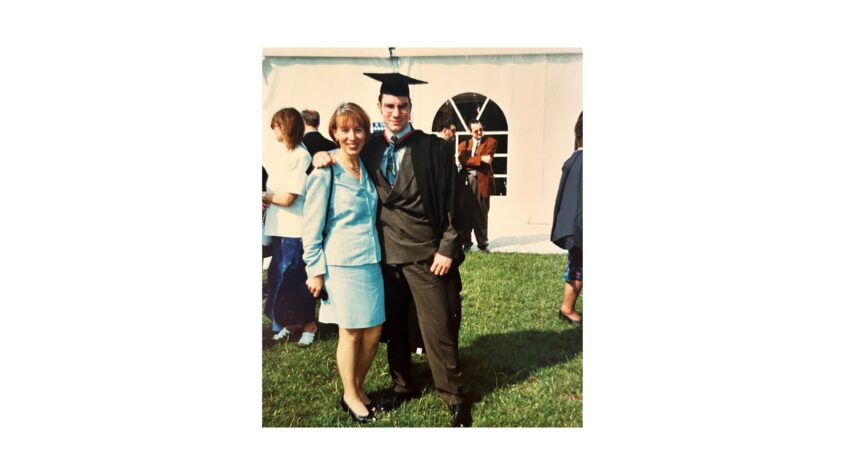 Woman and young man outside in front of marquee, man is wearing his graduation clothes
